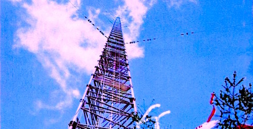 A view of a radio tower from the base of the tower. The sky is blue with a white cloud.